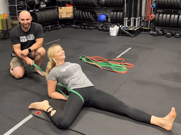 Coach Paul uses a resistance band for banded hip distraction during a private Rehab Training session at Sand & Steel Fitness